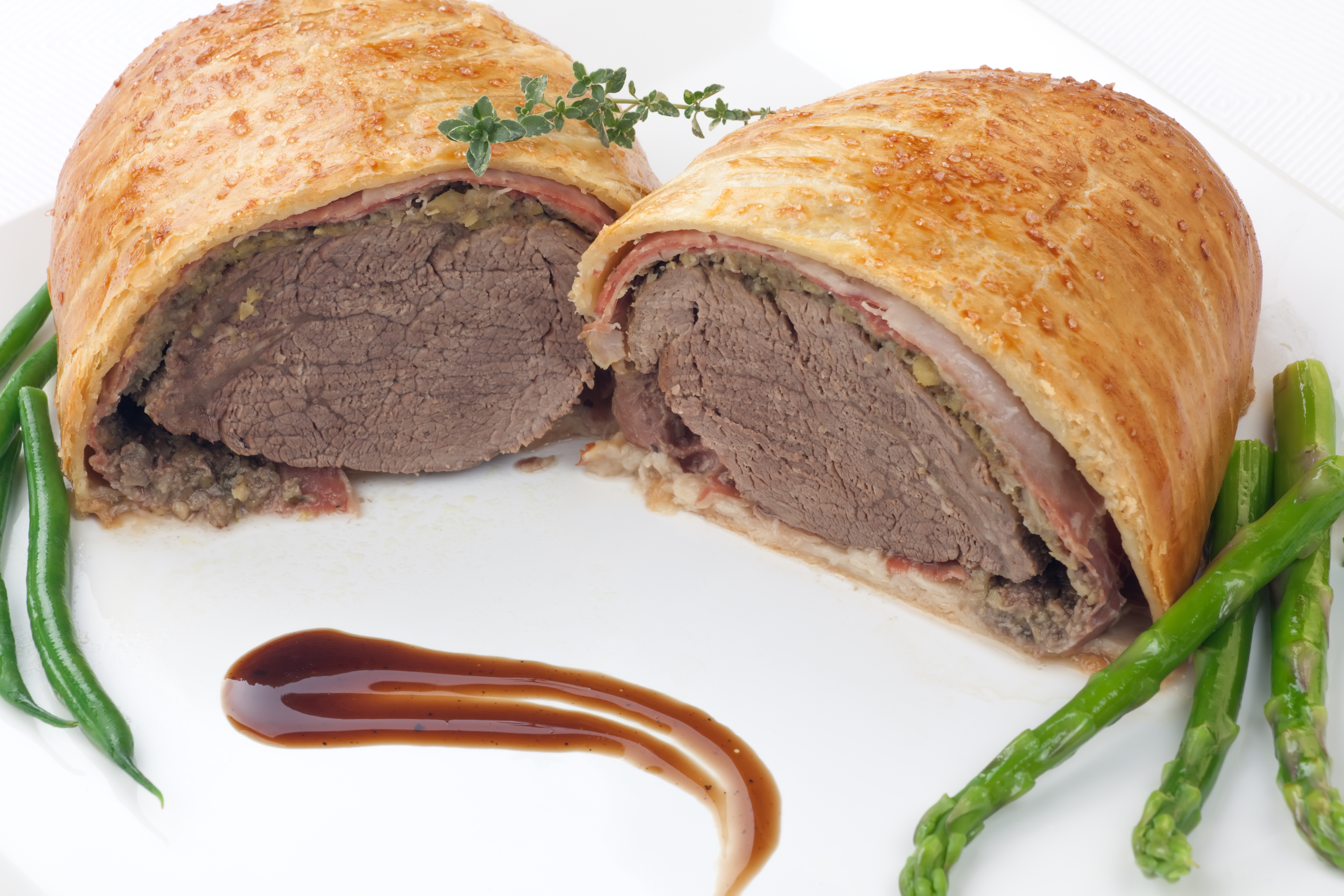 Beef Wellington - delicious roasted beef tenderloin rolled in mushroom puree and prosciutto then wrapped in puff pastry. Garnished with green beans tomatoes and asparagus.